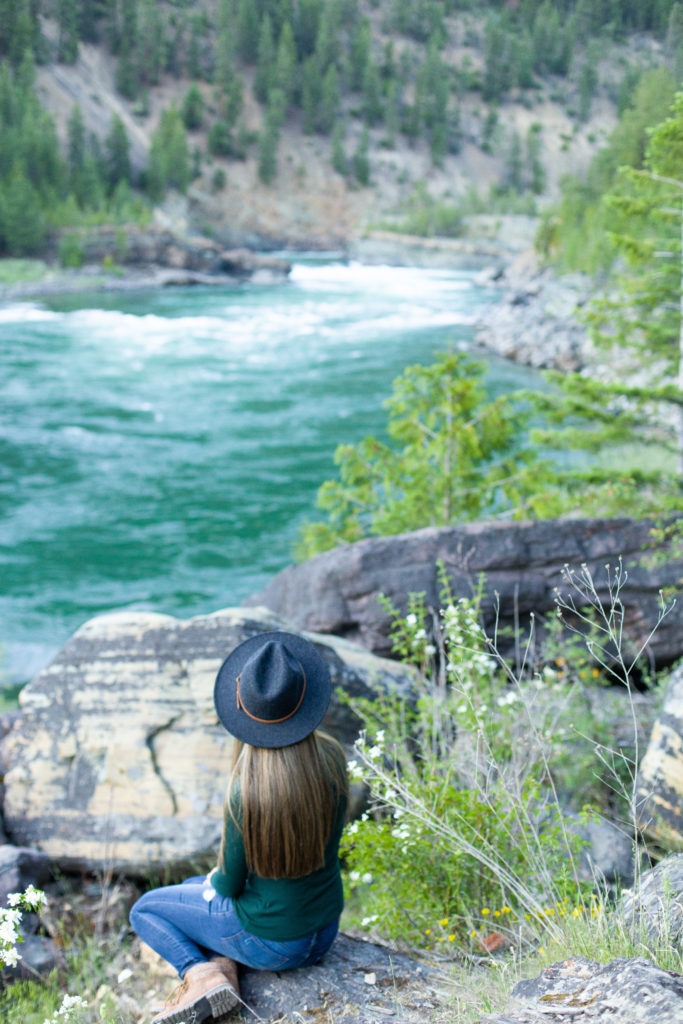girl in hat sitting on rock at kootenai falls 